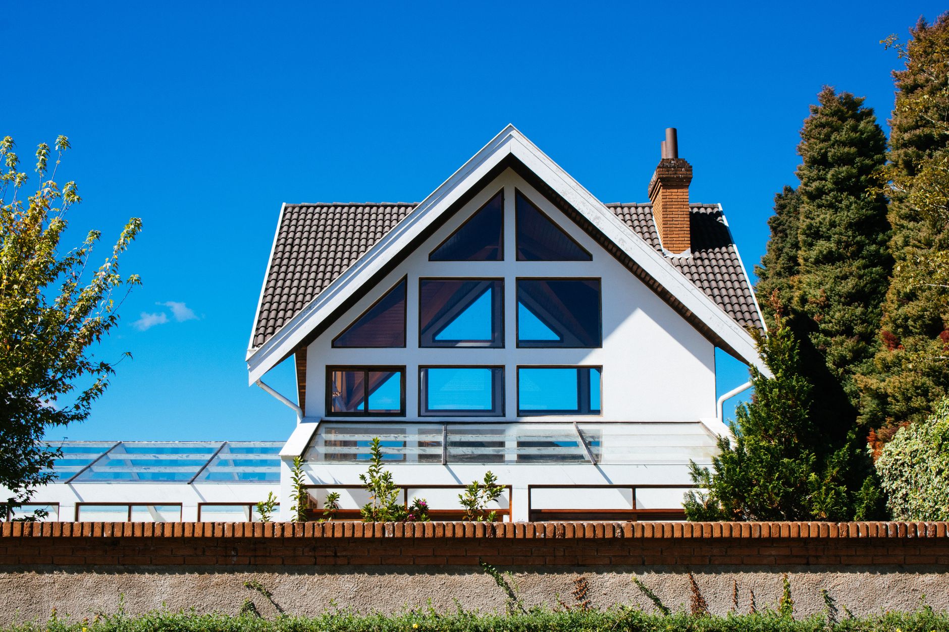 Contemporary A-frame house with large glass windows on a sunny day, surrounded by greenery