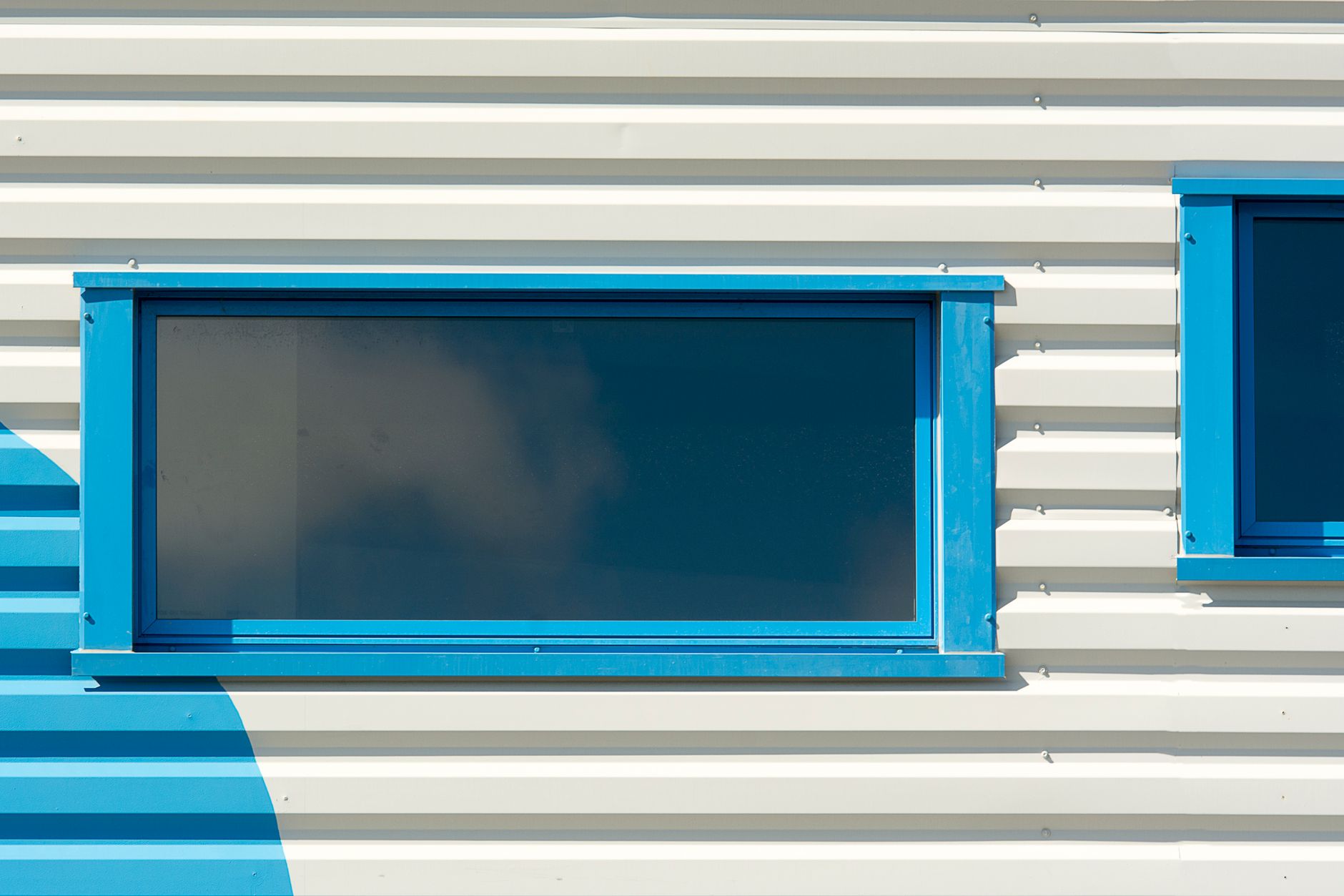 Close-up of a modern blue-framed window on a white corrugated building facade, highlighting urban design